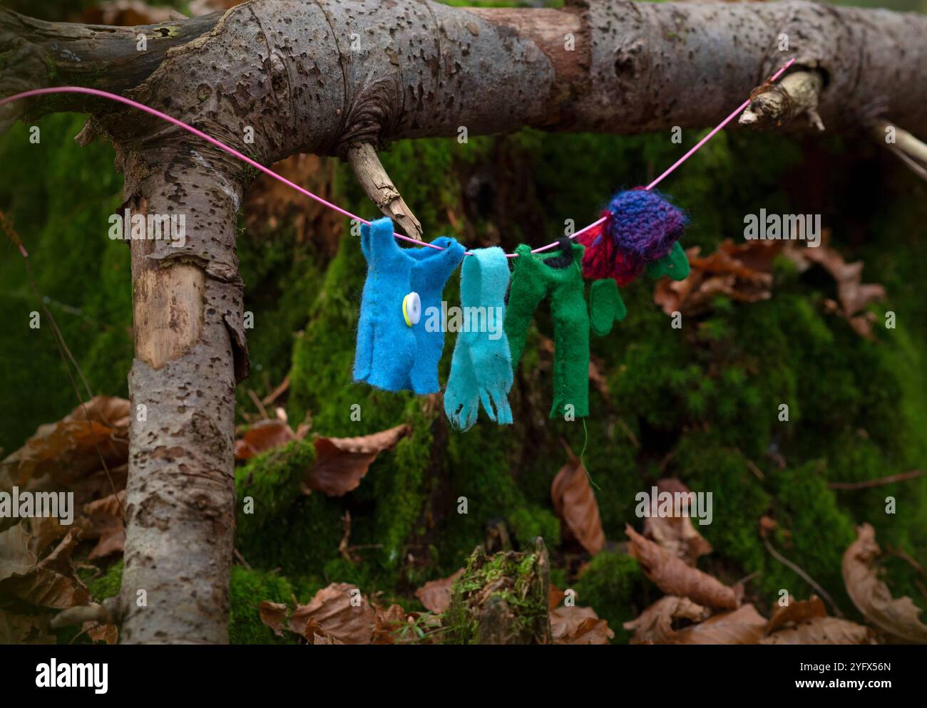Eine skurrile Präsentation winziger, farbenfroher Kleidung, die an einer Linie in einem Wald hängt und die Illusion einer Feen- oder Zwergwäsche erzeugt. Die Miniatur Stockfoto