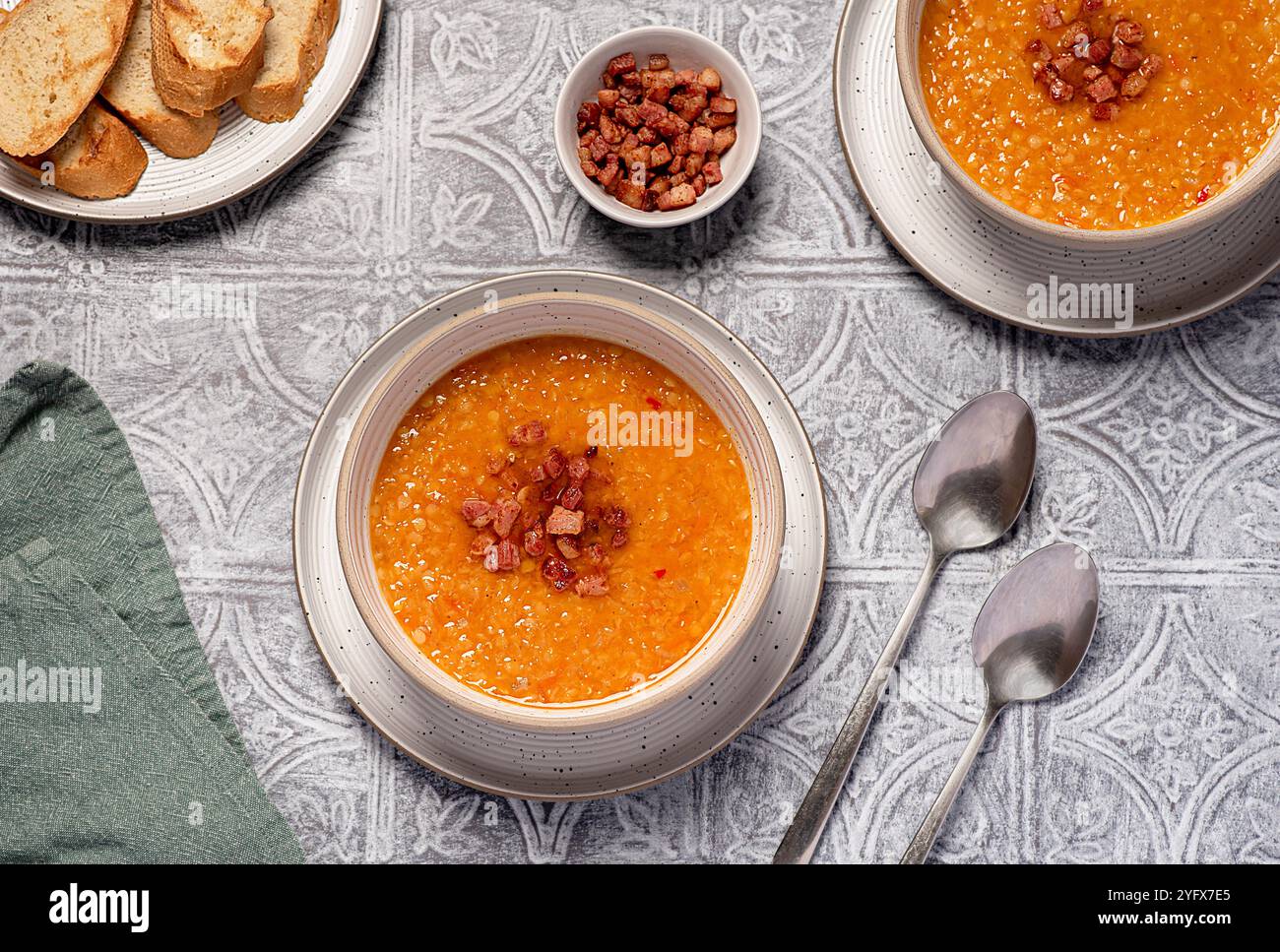 Lebensmittelfotografie von roter Linsensuppe mit Chili und Speck, Karotten, Zwiebeln, Knoblauch, geröstetem Brot, Brühe, Brühe, Set-Tisch Stockfoto