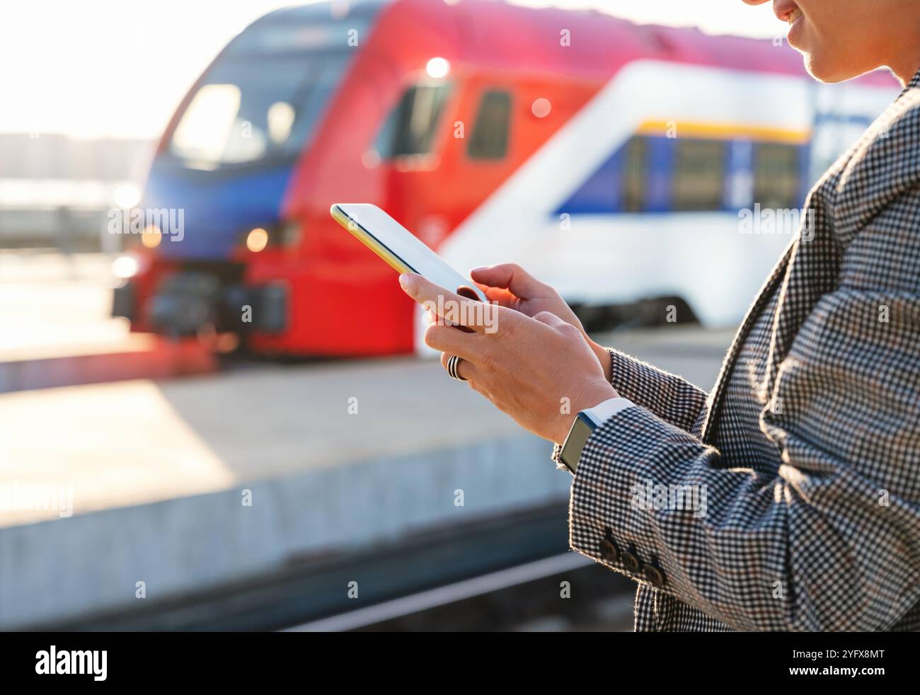 Online-Buchung von Zugtickets. Smartphone in den Händen einer Geschäftsfrau gegen einen unscharfen Zug auf dem Bahnsteig. Stockfoto