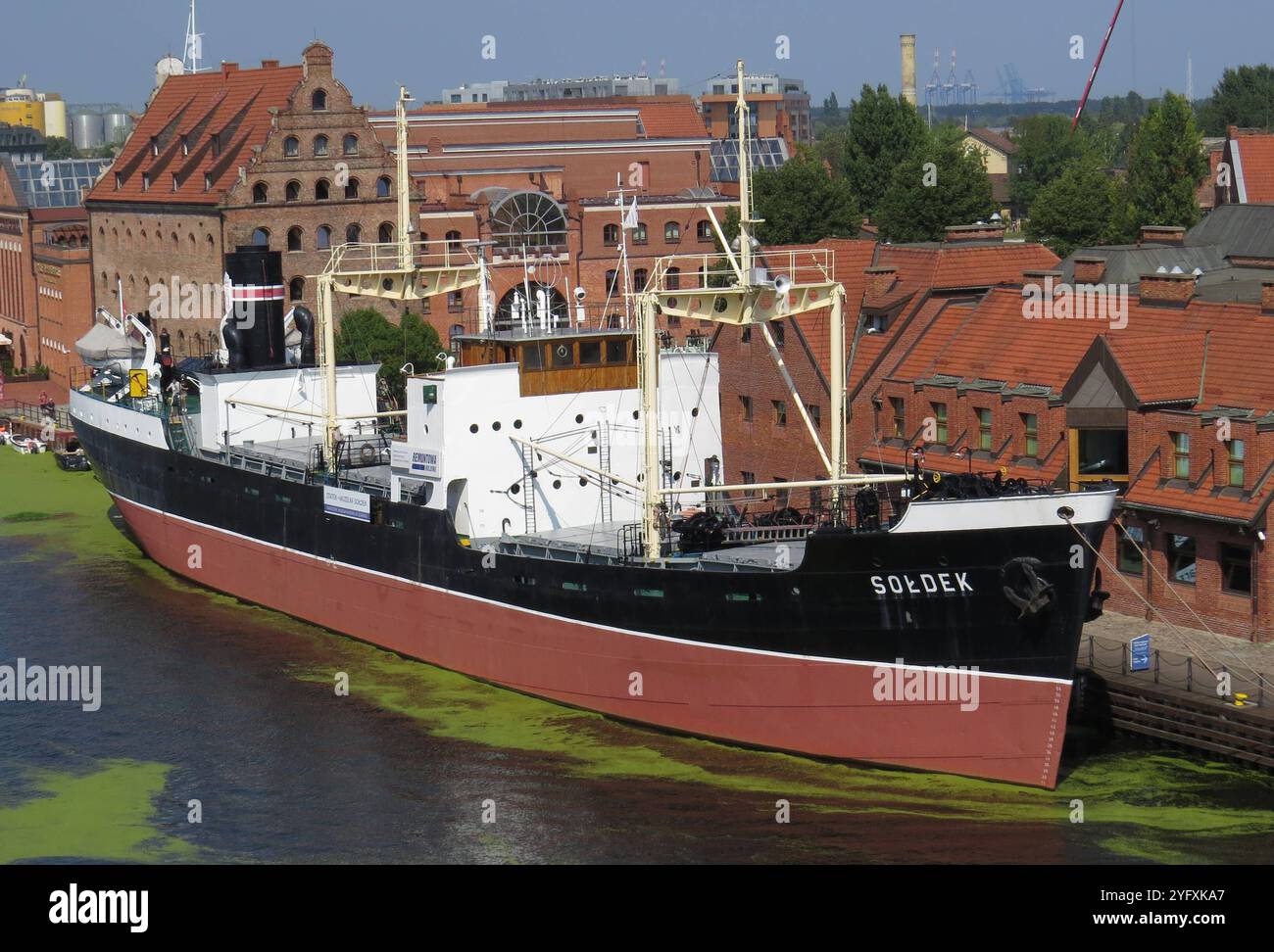 Symbolbild Museumsschiff Soldek im Hafen, erste polnische Seeschiff nach dem Zweiten Weltkrieg, liegt vor historischem Backsteingebaeuden, roter Dachziegel und Industriearchitektur im Hintergrund, gruene Algen auf Wasseroberflaeche, maritime Sehenswuerdigkeit in Danzig, Symbol für Polens Schiffbaugeschichte, Touristenattraktion, restauriertes Dampfschiff *** Symbolbild Museumsschiff Soldek im Hafen, erstes polnisches Seesschiff nach dem Zweiten Weltkrieg auf der Industriebau Stockfoto