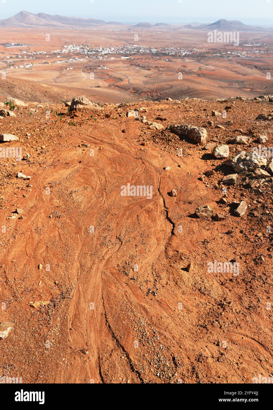 Vulkanische Wüstenlandschaft mit roter felsiger Oberfläche im trockenen Tal unter blauem Himmel. Wandern durch Fuerteventura. Kanarische Inseln, Spanien. Stockfoto