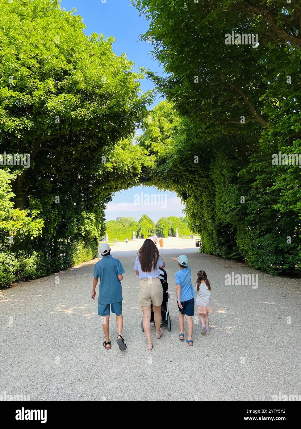 Eine Familie genießt einen gemütlichen Spaziergang durch einen lebendigen grünen Park unter klarem blauen Himmel im Schloss Schönbrunn, Österreich. Die Szene fängt das Wesen von ein Stockfoto