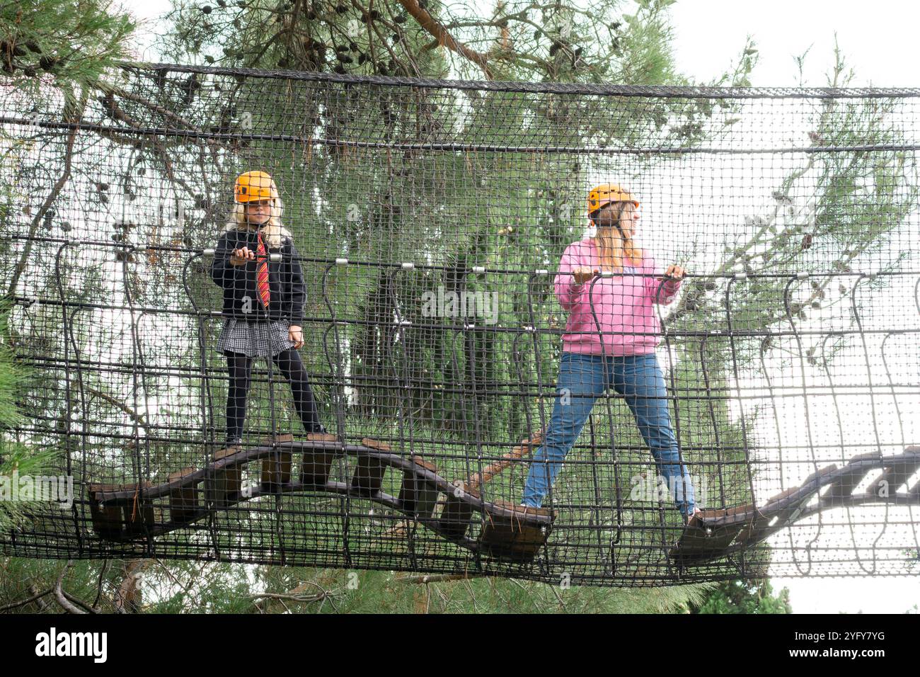 Abenteuerpark Kids Seilbrücke zwei Kinder mit Schutzhüten stehen auf einer Seilbrücke in einem Abenteuerpark. Stockfoto