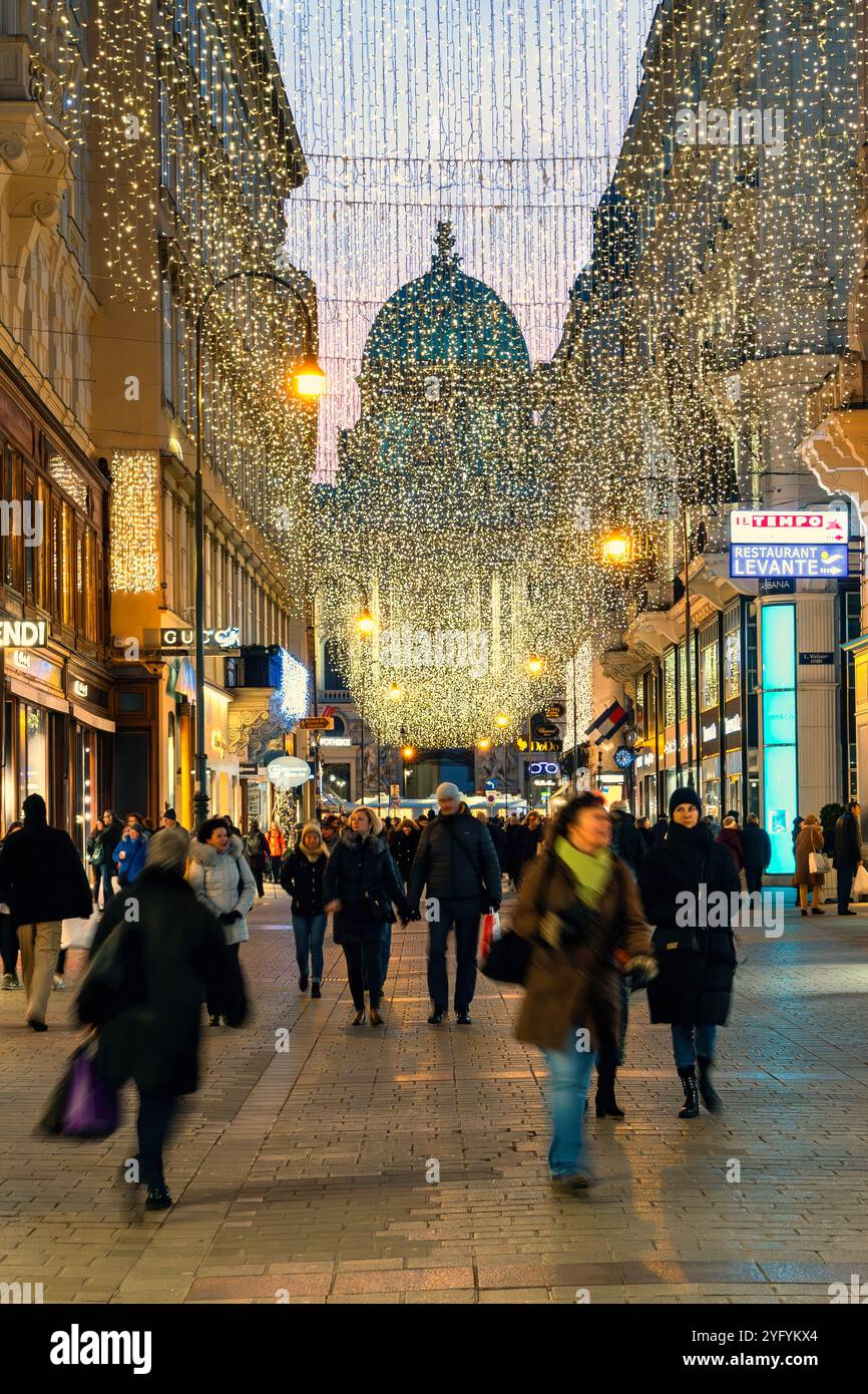 Menschen, die abends in Wien auf einer Fußgängerzone mit Weihnachtsbeleuchtung spazieren gehen. Stockfoto