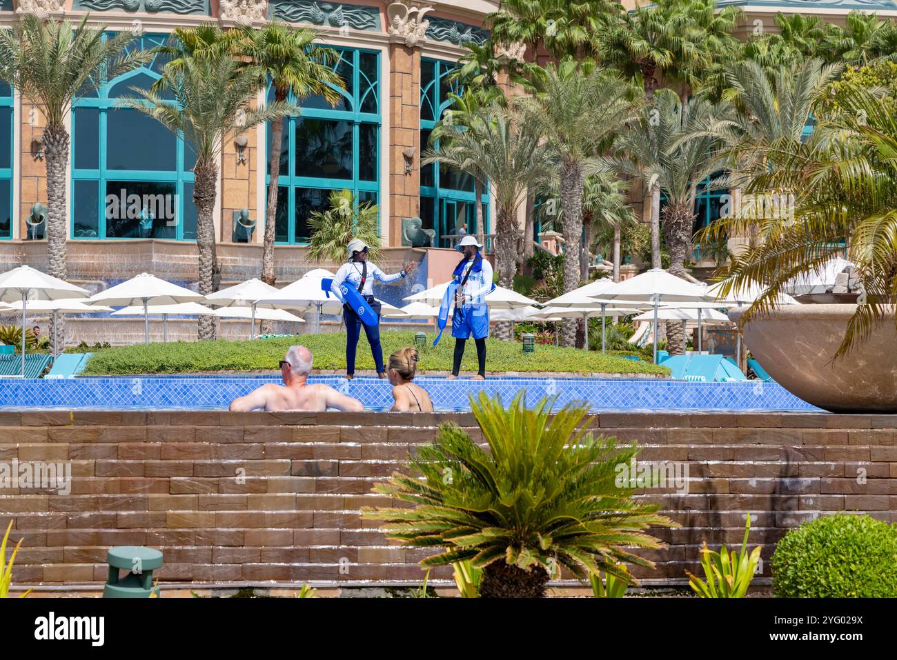 Hotelgäste kühlen sich im Royal Pool des Atlantis the Palm Hotels ab, der von zwei Badeschwimmern bewacht wird Stockfoto