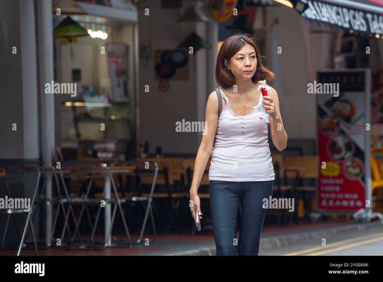 Eine Chinesin Japanerin, 40-50 Jahre alt, mit Eiscreme-Dessertkegel, die allein in der Sago Street, Chinatown, Singapur, wandert. Stockfoto