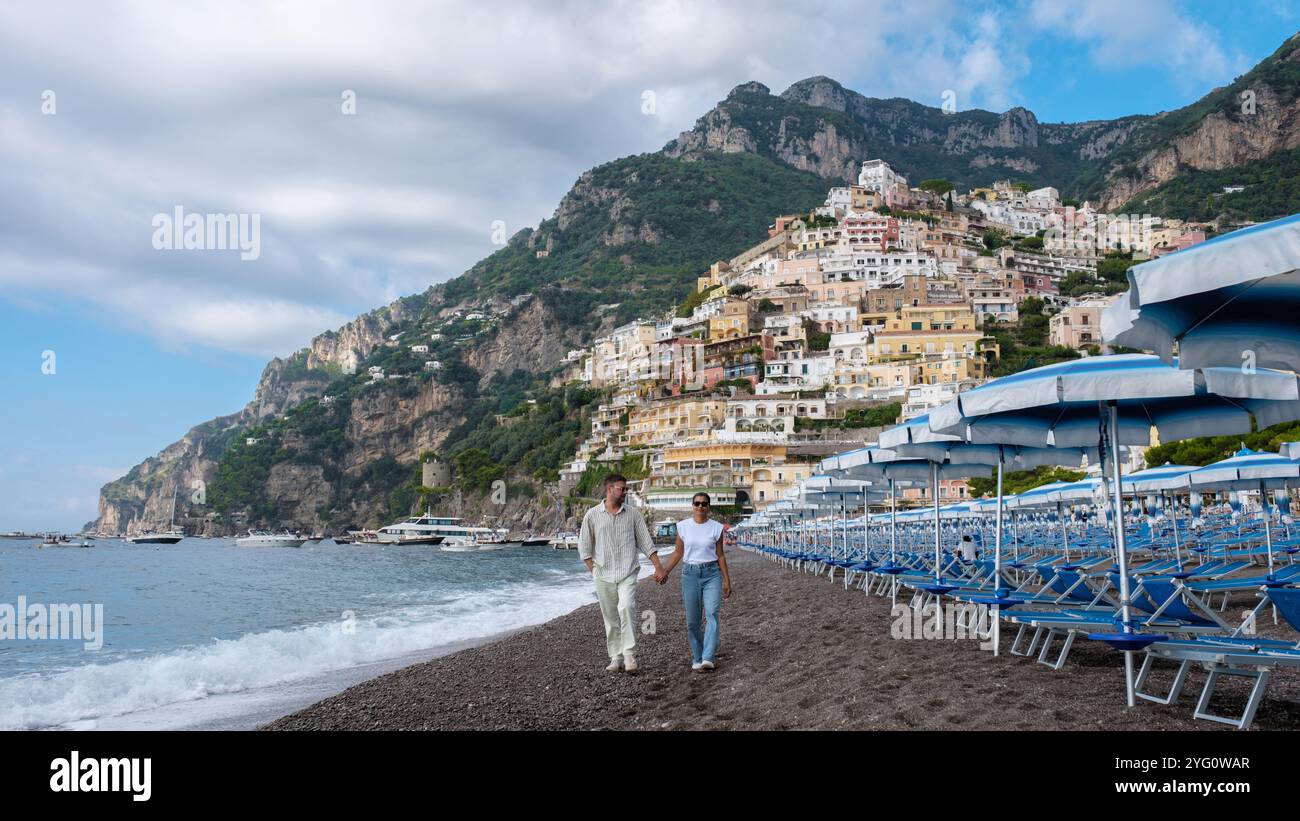 Ein Paar genießt einen gemütlichen Spaziergang am Kiesstrand von Positano, mit farbenfrohen Villen an den Klippen und einer lebhaften Küstenatmosphäre, die ihre romantik unterstreicht Stockfoto