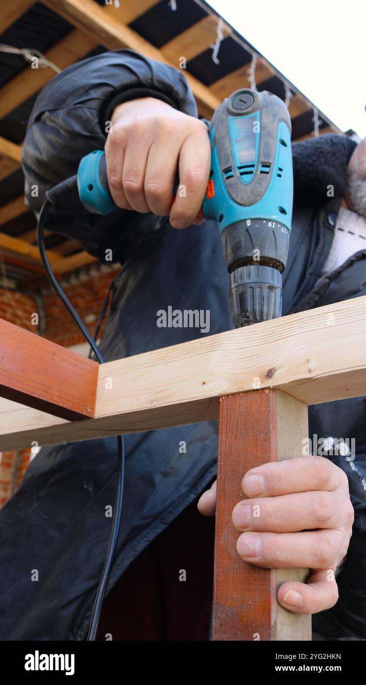 Der Arbeiter verwendet einen Schraubendreher, um eine selbstschneidende Schraube in eine Holzkonstruktion zu bohren oder zu Schrauben, während er sie mit einer Hand hält Stockfoto