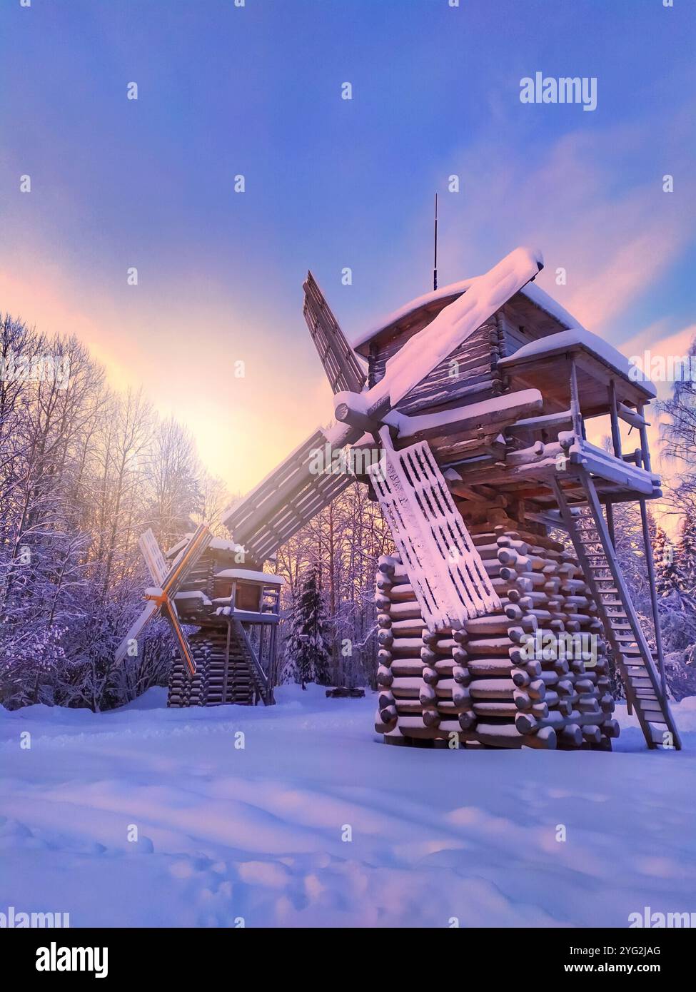 Eine Windmühle aus Holz steht im Schnee. Der Himmel ist eine wunderschöne Mischung aus Blau und Rosa, die eine ruhige und friedliche Atmosphäre schafft. Stockfoto