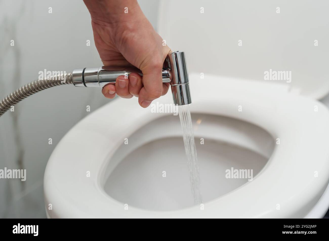 Hand mit Chrom-Bidet-Dusche in einer Toilettenschüssel Stockfoto