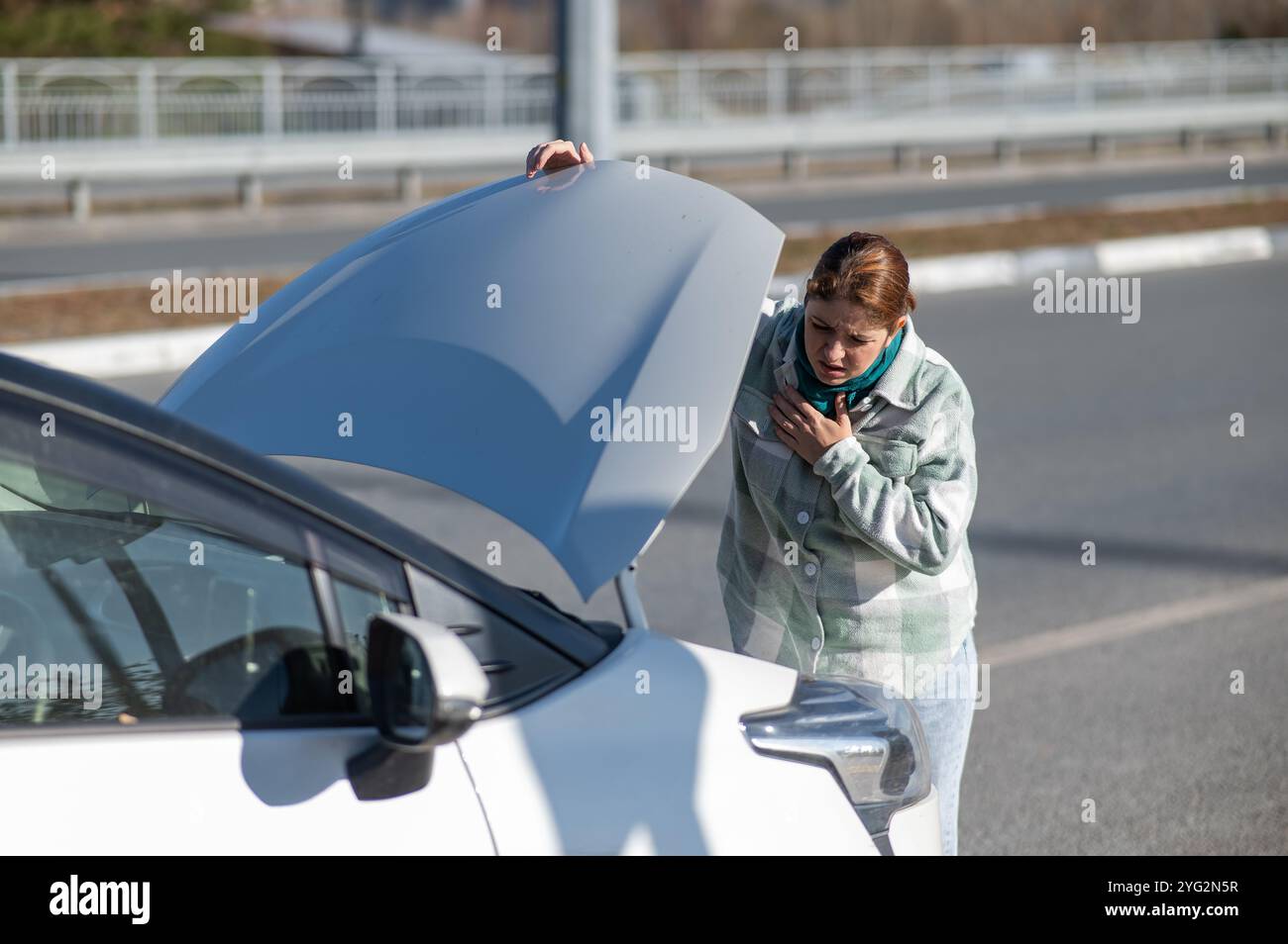 Die kaukasische Frau sieht unter der Motorhaube eines Autos verwirrt aus. Stockfoto