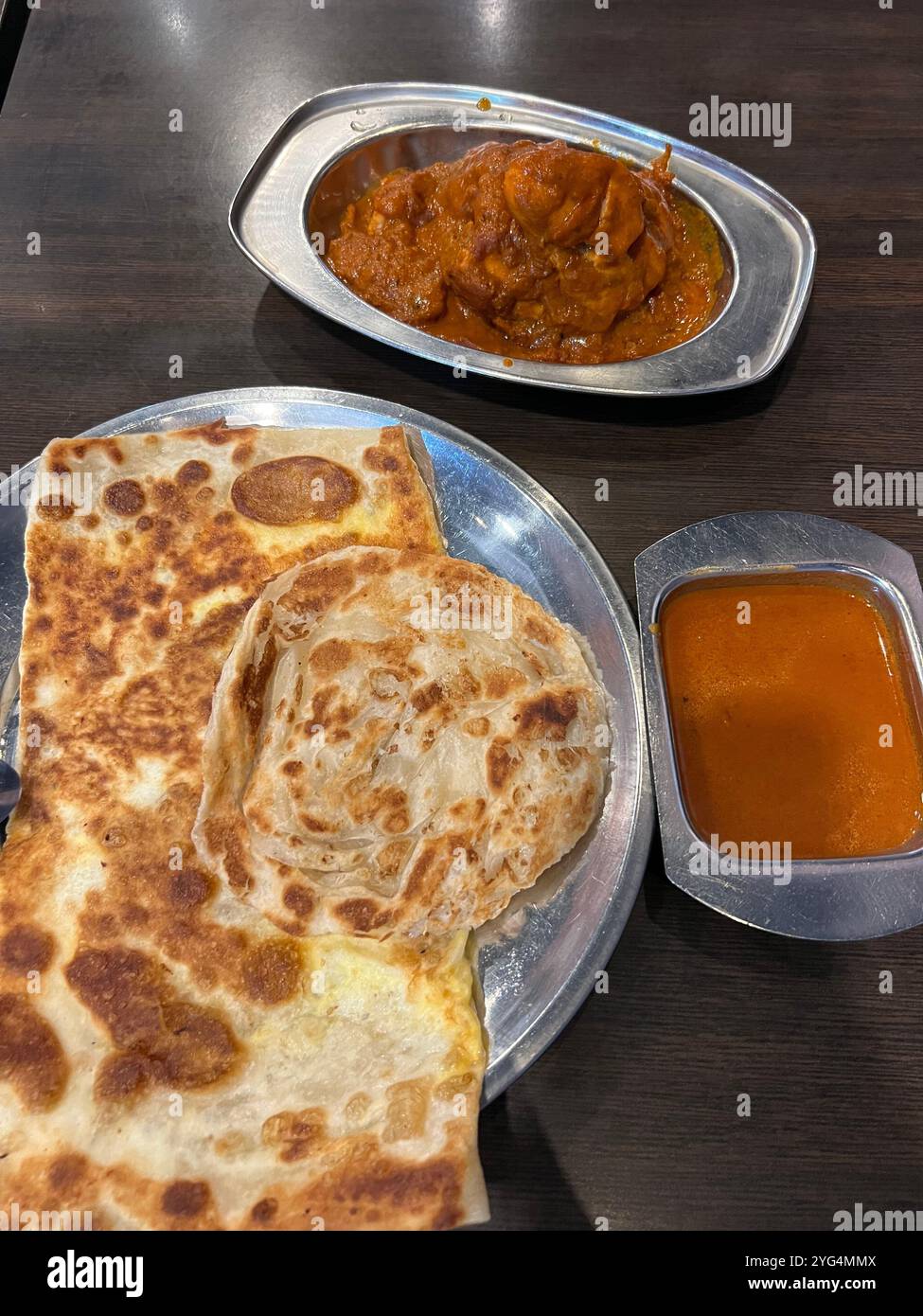 Food-Shot-Präsentation mit reinem und Ei Roti Prata, einem Teller mit Fisch-Curry, einem Teller mit Masala-Huhn in normaler Größe zum Abendessen. Singapur. Stockfoto