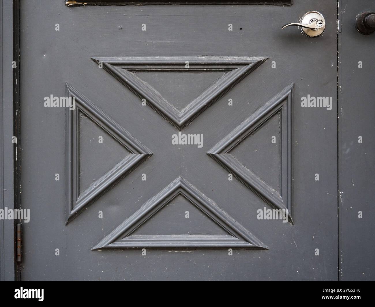 Dekorative graue Tür mit einzigartigem geometrischem Design und poliertem Griff in einem gepflegten Eingangsbereich Stockfoto