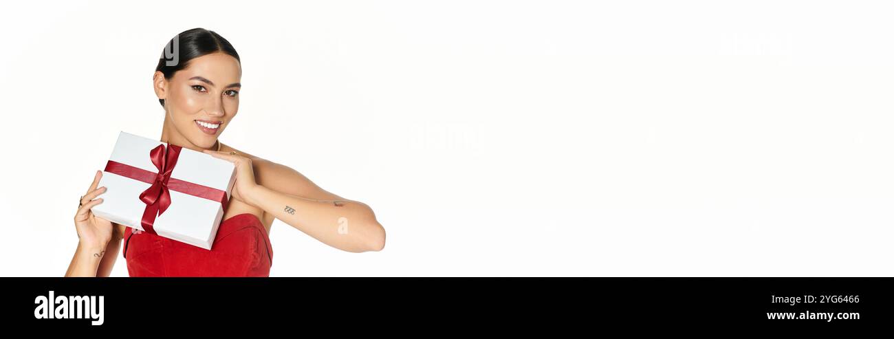Eine junge Frau mit einem strahlenden Lächeln präsentiert ein wunderschön gewickeltes Geschenk in einem eleganten Raum Stockfoto