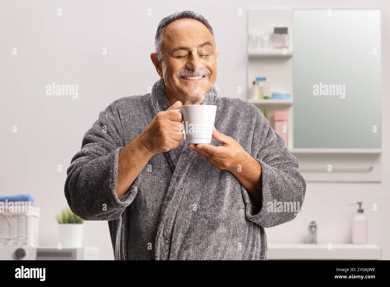 Glücklicher reifer Mann im Bademantel, der zu Hause eine Tasse heißes dampfendes Getränk genießt Stockfoto