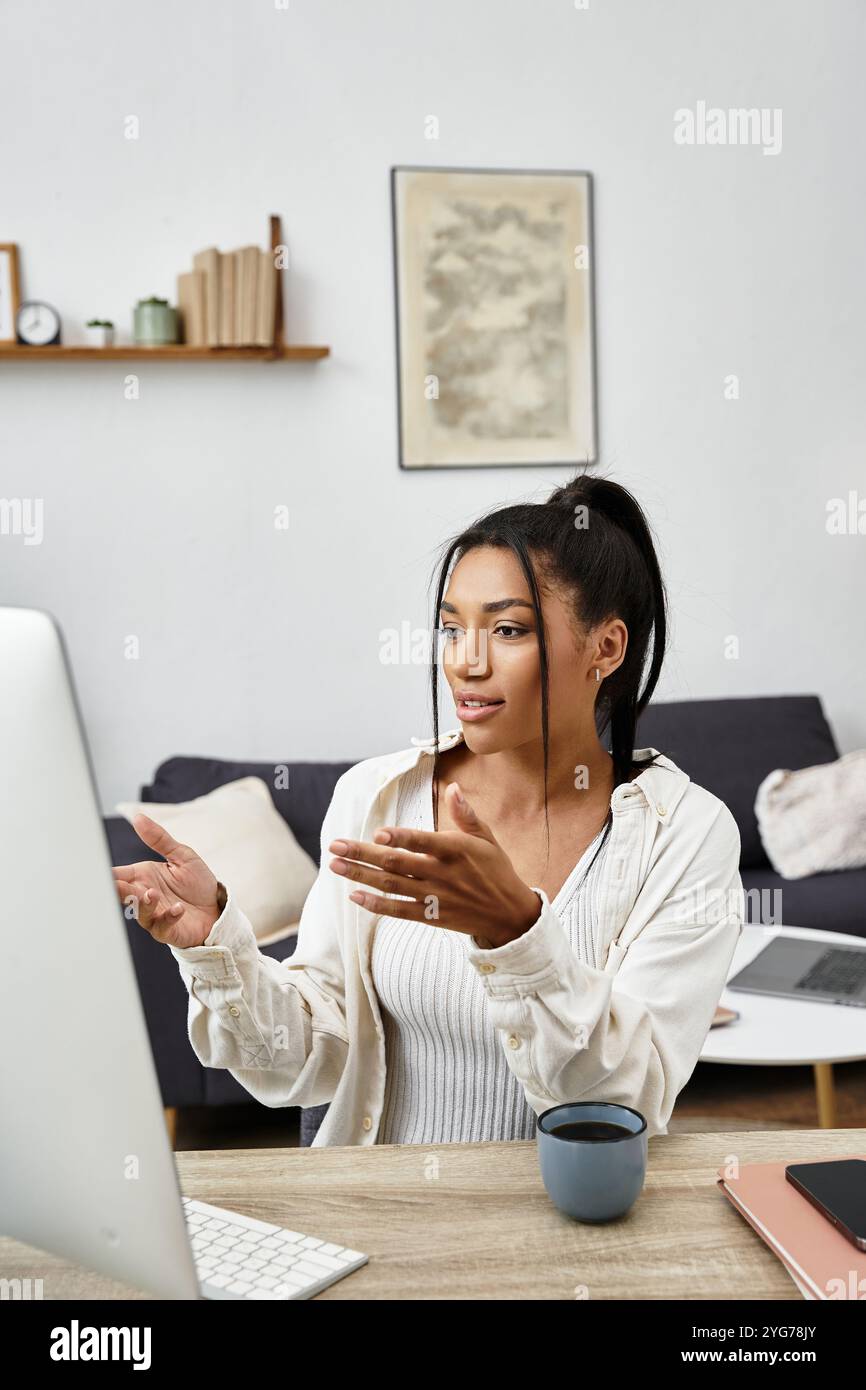 Eine junge Frau lernt aktiv von zu Hause aus, arbeitet mit ihrem Computer und genießt einen warmen Drink. Stockfoto