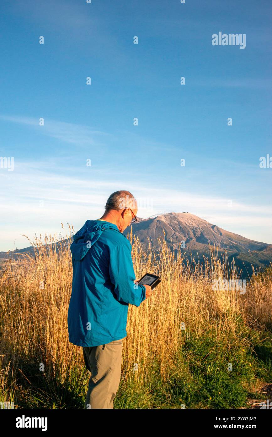 Erwachsene ältere Männer entspannen sich, während sie ein kindle-Buch mit Mount Saint Helensin im Hintergrund lesen. Northern Cascades, Bundesstaat Washington. USA Stockfoto