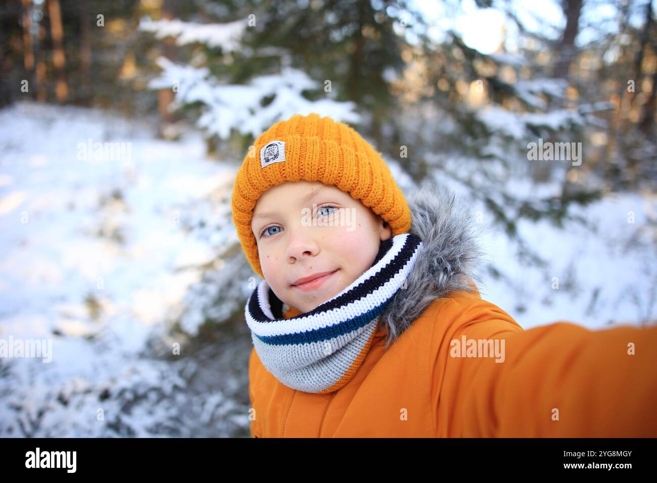 Ein entzückendes Porträt eines Kindes, das glücklich ein Selfie in einem verschneiten Wald macht. Stockfoto