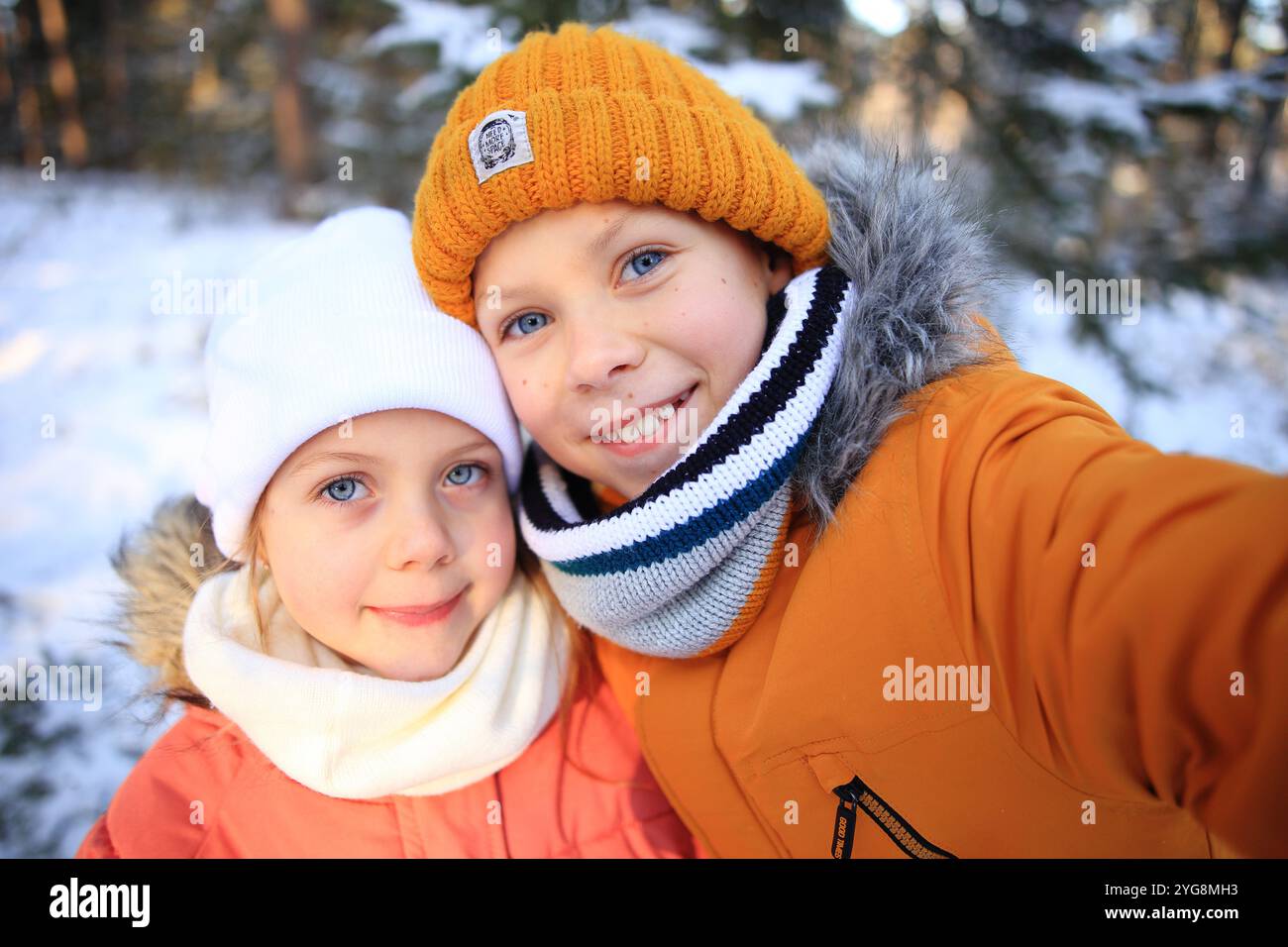 Eine lebhafte Szene, in der Kinder glücklich ein Selfie vor einem malerischen, verschneiten Wald machen. Ihr helles Lächeln und ihre verspielten Posen spiegeln die Freude an wi wider Stockfoto