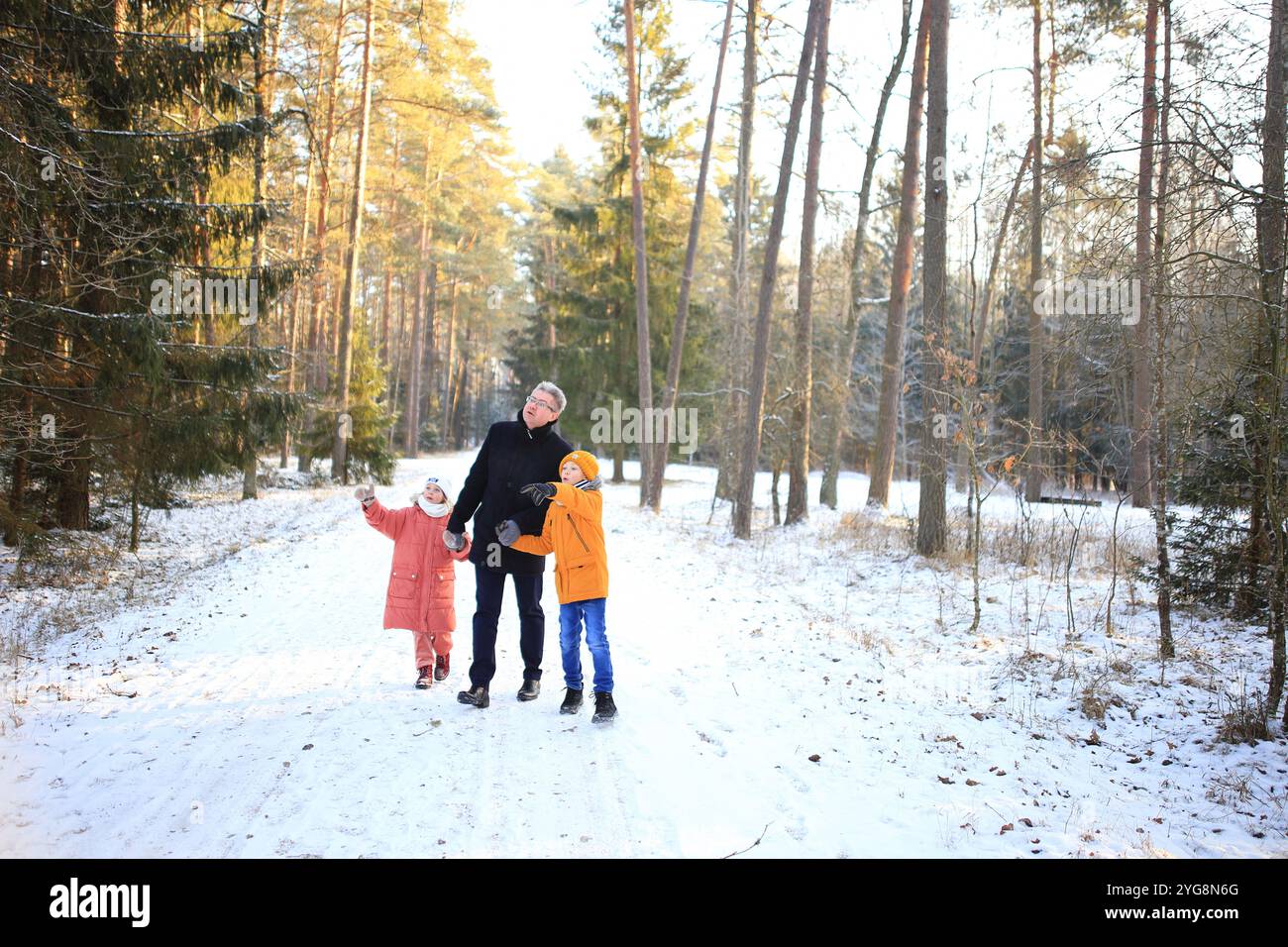 Ein Vater macht einen gemütlichen Spaziergang mit seinen beiden Kindern durch einen wunderschönen verschneiten Wald. Die Szene fängt die Freude der Familie in der ruhigen W ein Stockfoto