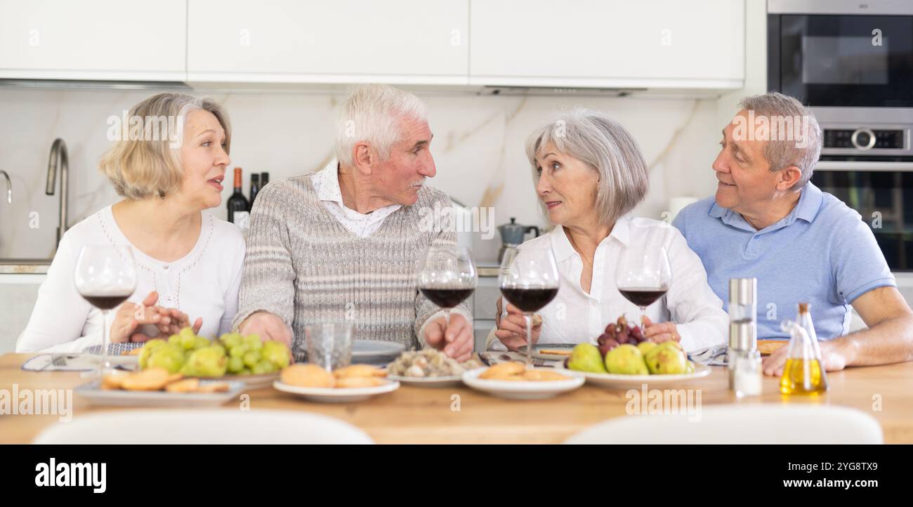 Zwei ältere Ehepaare sitzen am Tisch, genießen Essen und Wein, plaudern. Stockfoto