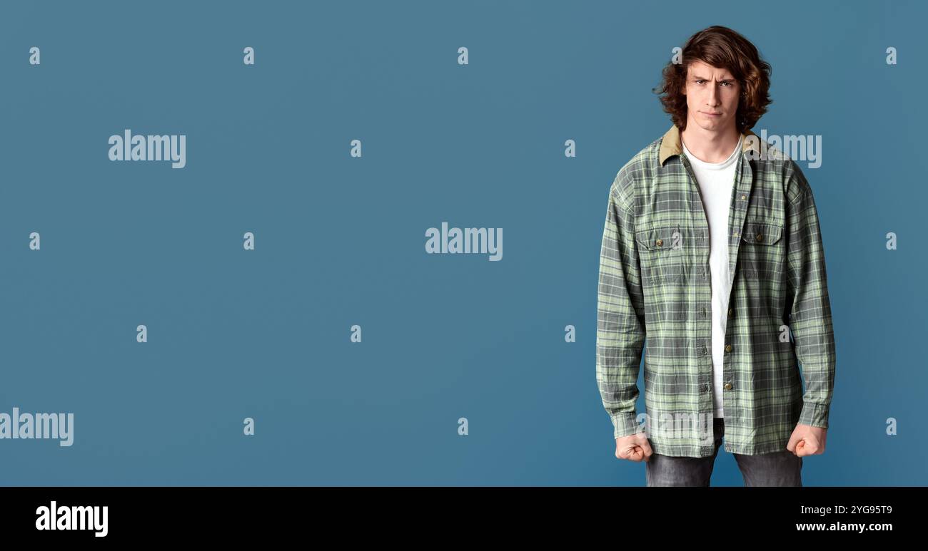 Junger Mann, der seine Fäuste in Wut zusammenklammert und auf türkisfarbenem Hintergrund die Stirn runzelt Stockfoto