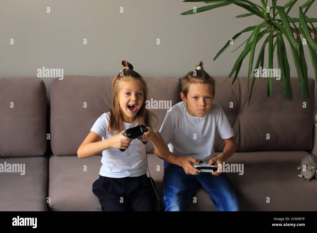 Eine lebendige Szene, in der ein Junge und ein Mädchen zu Hause gemeinsam Videospiele spielen. Sie tauchen in das Gaming-Erlebnis ein und heben hervor Stockfoto