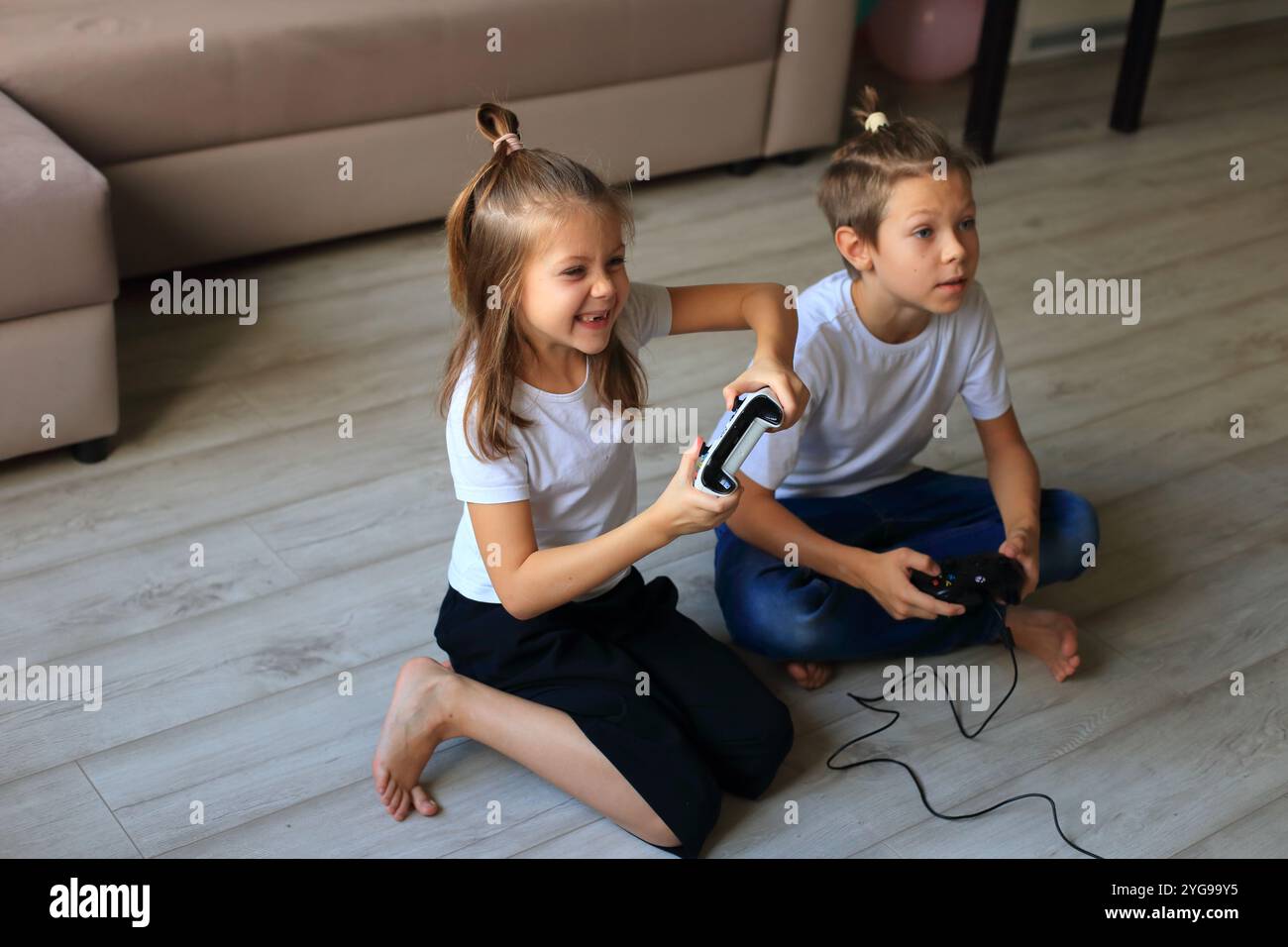 Eine lebendige Szene, in der ein Junge und ein Mädchen zu Hause gemeinsam Videospiele spielen. Sie tauchen in das Gaming-Erlebnis ein und heben hervor Stockfoto