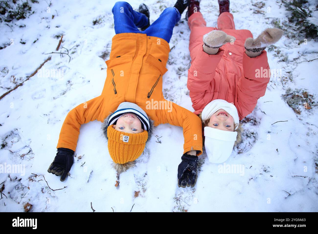 Eine fröhliche Szene fängt Kinder ein, die in einer weichen Schneedecke liegen, während ihr Lachen und ihre verspielten Mätzchen die Luft füllen. Stockfoto