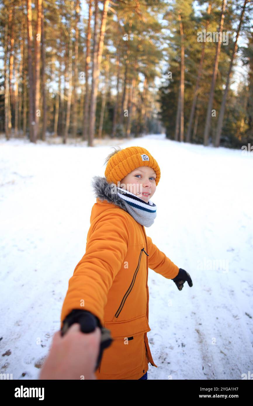 Ein junger Mann spaziert gemütlich durch einen malerischen, verschneiten Wald, umgeben von hoch aufragenden Bäumen, die mit frischem Schnee bedeckt sind. Stockfoto