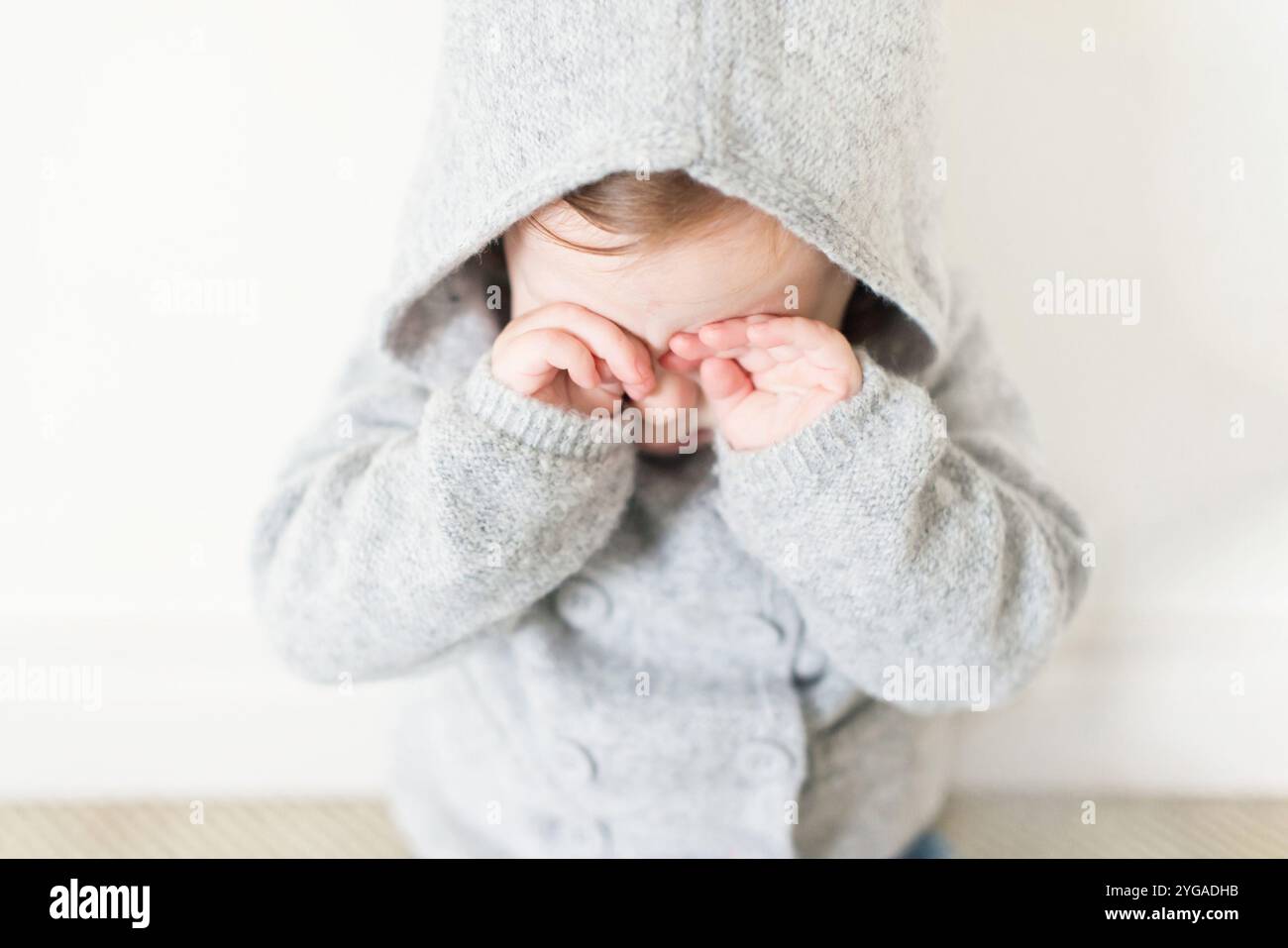 Baby in einem grauen Kapuzenpullover, der die Augen bedeckt Stockfoto Baby in einem grauen Kapuzenpullover, der die Augen bedeckt Stockfoto