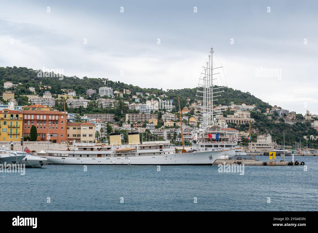 Nizza, Frankreich - 24.09.2024: Kleine Kreuzfahrtschiffe legen im Hafen von Port de Nizza an, mit Wohngebäuden am Hang im Hintergrund. Stockfoto