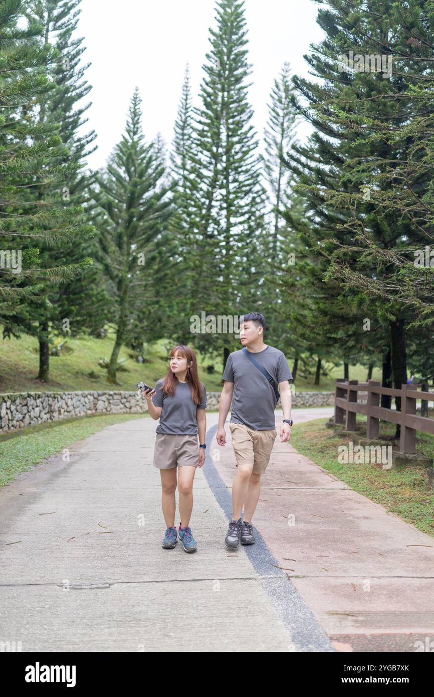 Ein chinesisch-malaysisches Paar in den 30ern spaziert zusammen in einem grünen Park mit reichlich Wasser in Kuala Lumpur, Malaysia, an einem sonnigen Tag im Juni 2024. Stockfoto