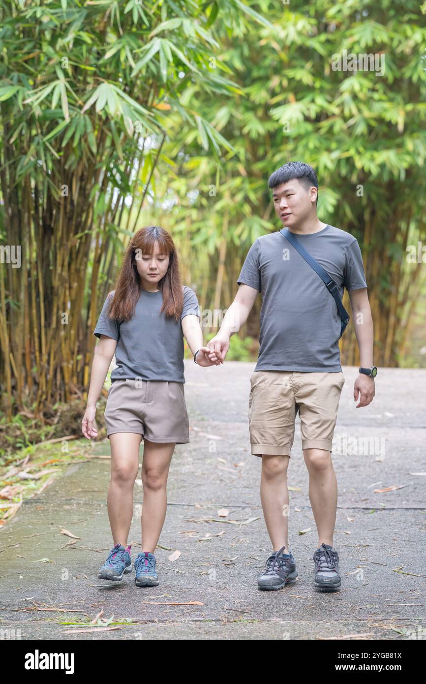 Ein chinesisch-malaysisches Paar in den 30ern spaziert zusammen in einem grünen Park mit reichlich Wasser in Kuala Lumpur, Malaysia, an einem sonnigen Tag im Juni 2024. Stockfoto