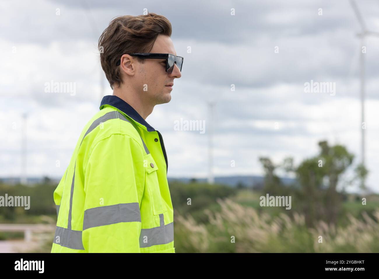 Intelligenter junger Ingenieur Techniker männlicher Arbeiter stehend Seitenansicht Nahaufnahme bei Wind Turbines Clean Power Generator Feld Hintergrund. Stockfoto