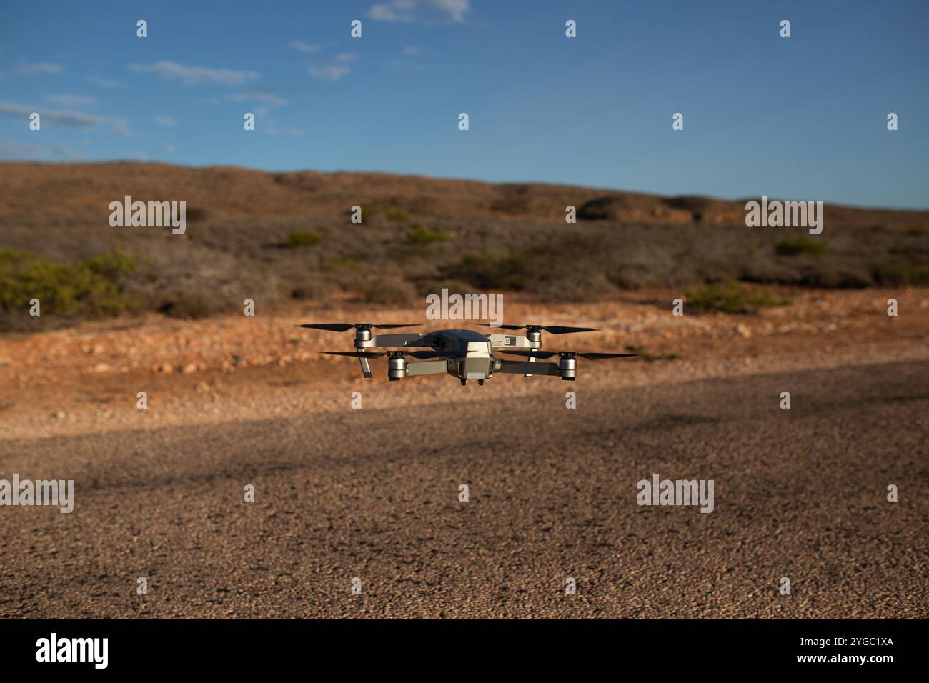 DJI-Drohne im Rahmen, schwebt über einer versiegelten Straße, kurz vor der Landung. Der australische Outback-Hintergrund ist verschwommen und zeigt roten Schmutz, Bus Stockfoto