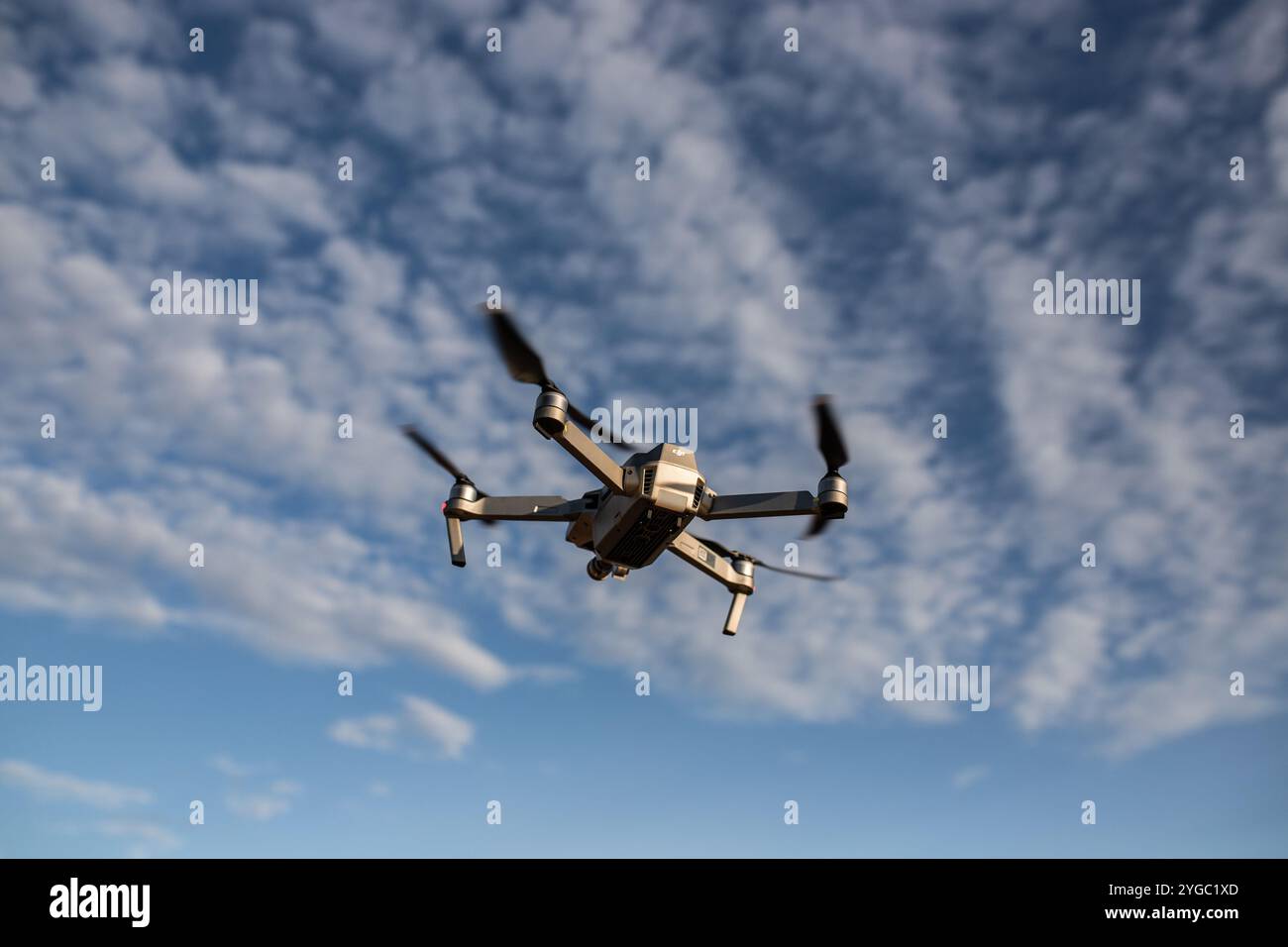 Foto einer DJI-Drohne, die im Rahmen zentriert ist und mit aufgenommenem Propellerimpuls in den Himmel fliegt. Aufgenommen zur goldenen Stunde mit verschwommenem Hintergrund Stockfoto