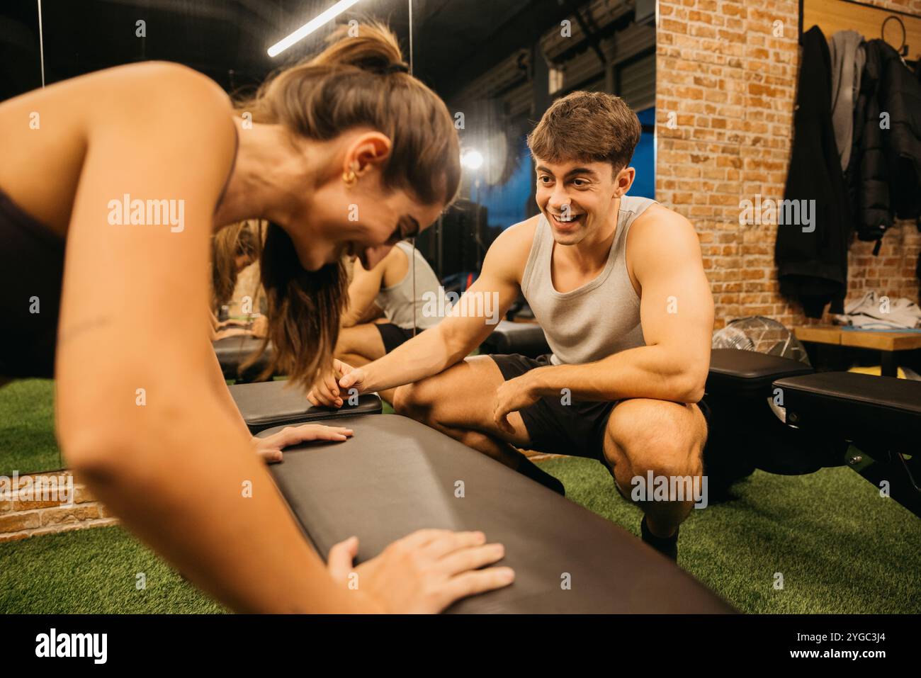 Ein junger Mann und eine junge Frau genießen gemeinsam ein lebhaftes Workout im Fitnessstudio. Ihr Lächeln und ihre Trainingsroutine betonen Fitness, Motivation und Freunde Stockfoto