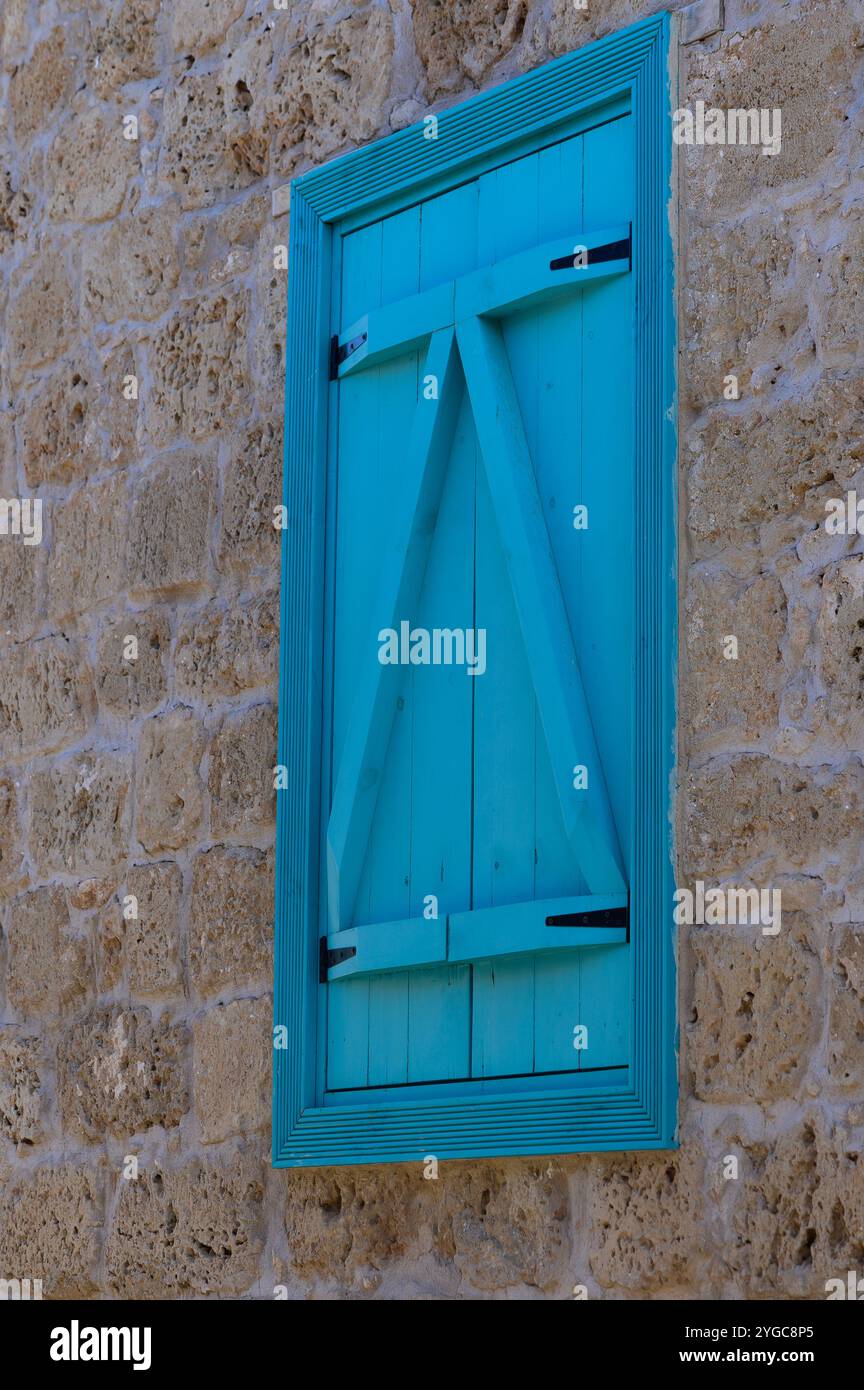 Ein markanter türkisfarbener Verschluss liegt an einer verwitterten Steinmauer und unterstreicht den Charme einer friedlichen Dorfatmosphäre. Stockfoto