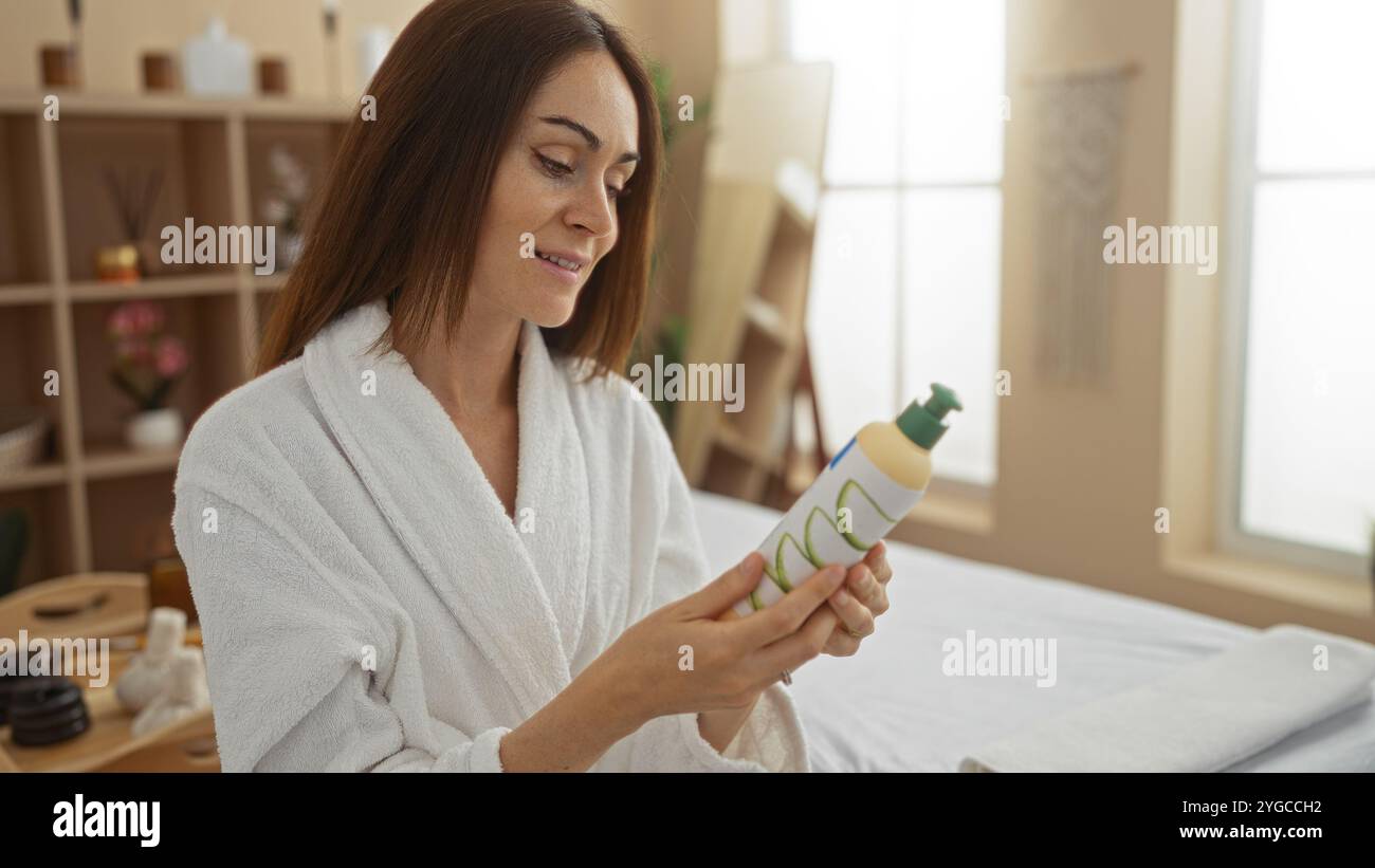 Junge Frau in einem Spa-Zimmer, die Kosmetikprodukte untersucht und gleichzeitig ein ruhiges Wellness-Erlebnis in einem gemütlichen Salon-Interieur genießt Stockfoto