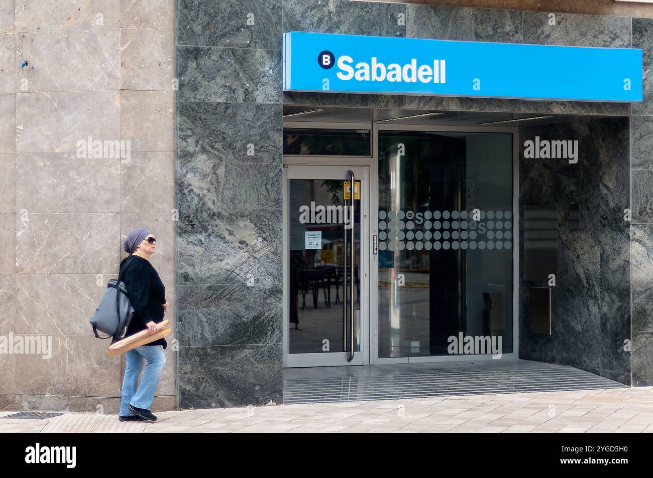 Viladecans. Spanien - 7. November 2024: Frau geht am Eingang der Sabadell Bank vorbei Stockfoto