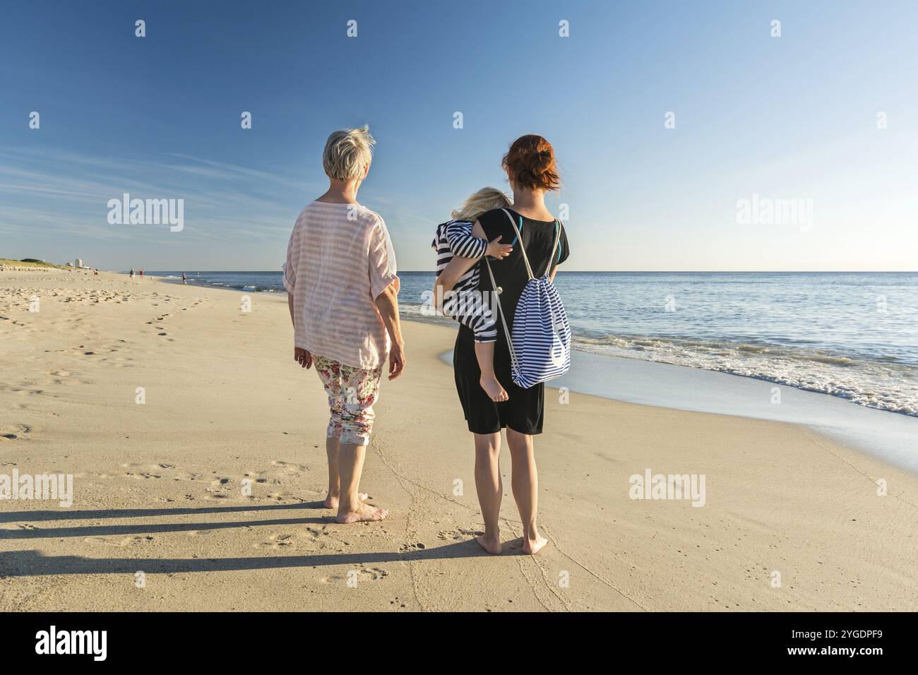 Junge und alte Frauen stehen am Strand in der Abendsonne und blicken zum Horizont Stockfoto