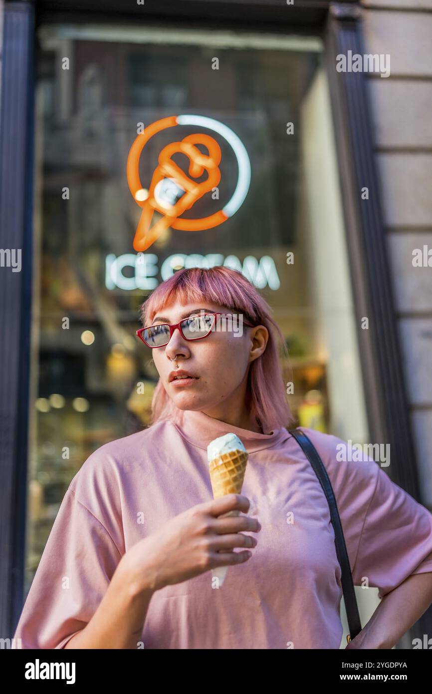 Moderne Millennials-Frau mit rosa Haaren und modernem Haarschnitt, die Eis in der Stadt isst Stockfoto