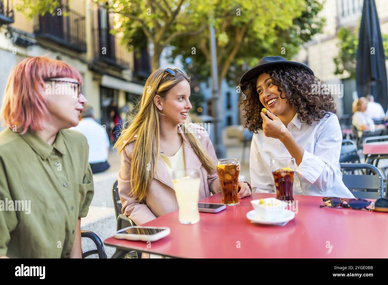 Moderne, vielfältige Frauen, die auf der Bar sitzen, trinken und essen Snacks in der Stadt Stockfoto