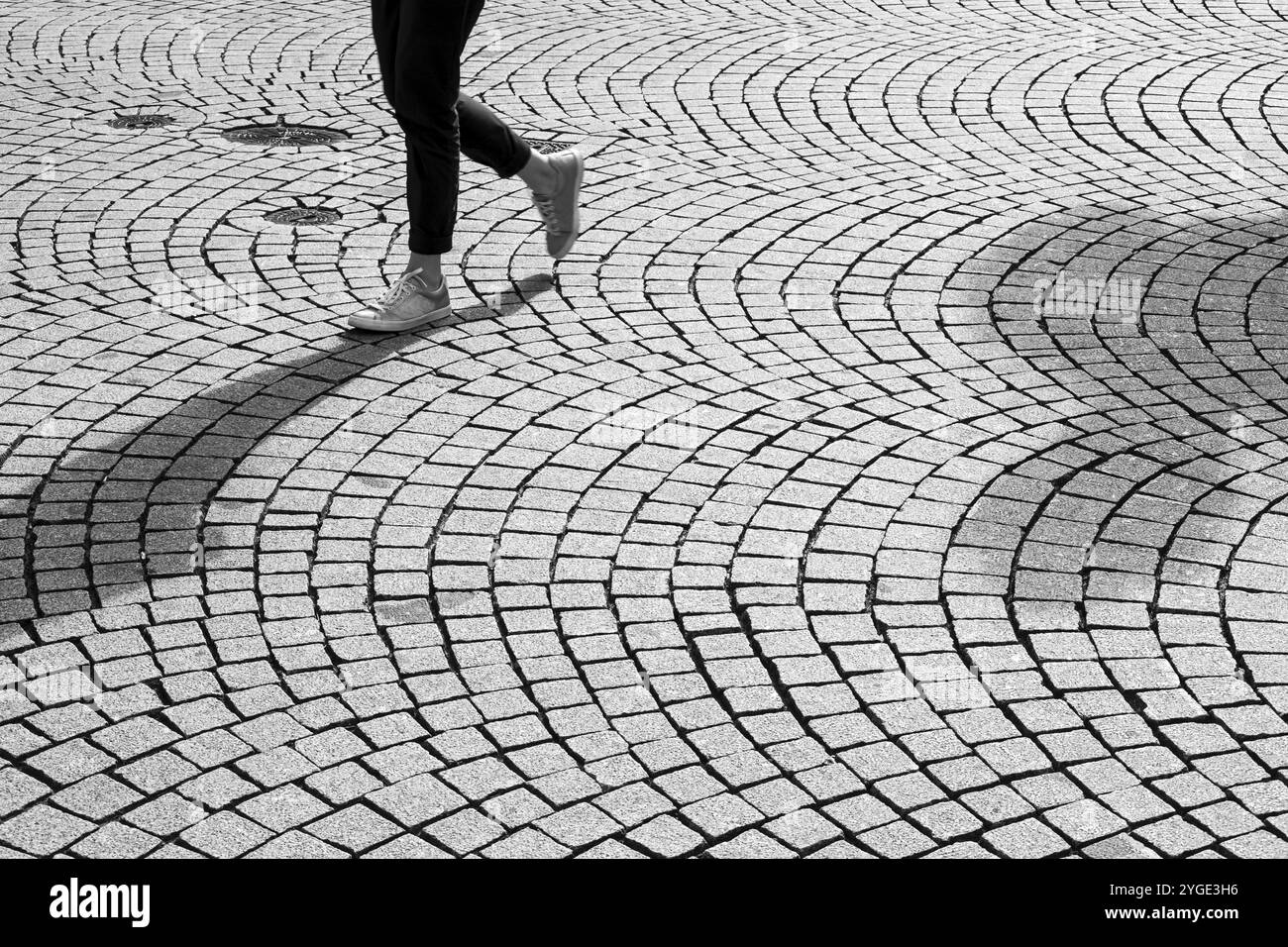 Füße und Beine einer Person, die auf einer gepflasterten Straße läuft Stockfoto