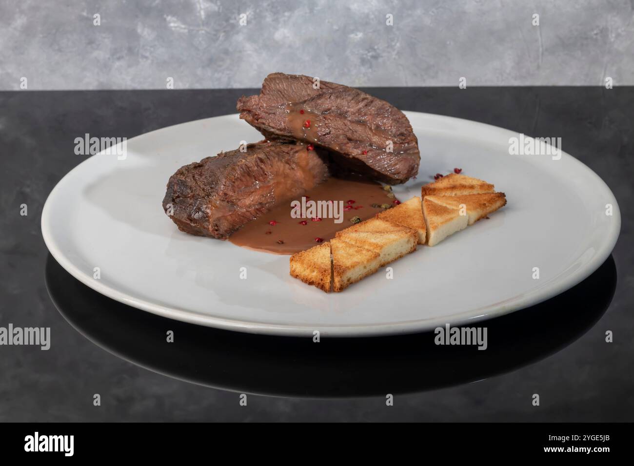 Gebackenes Rindfleisch mit Schokoladen-Wein-Sauce und Croutons. Fleisch auf einem weißen Teller. Menükonzept Stockfoto