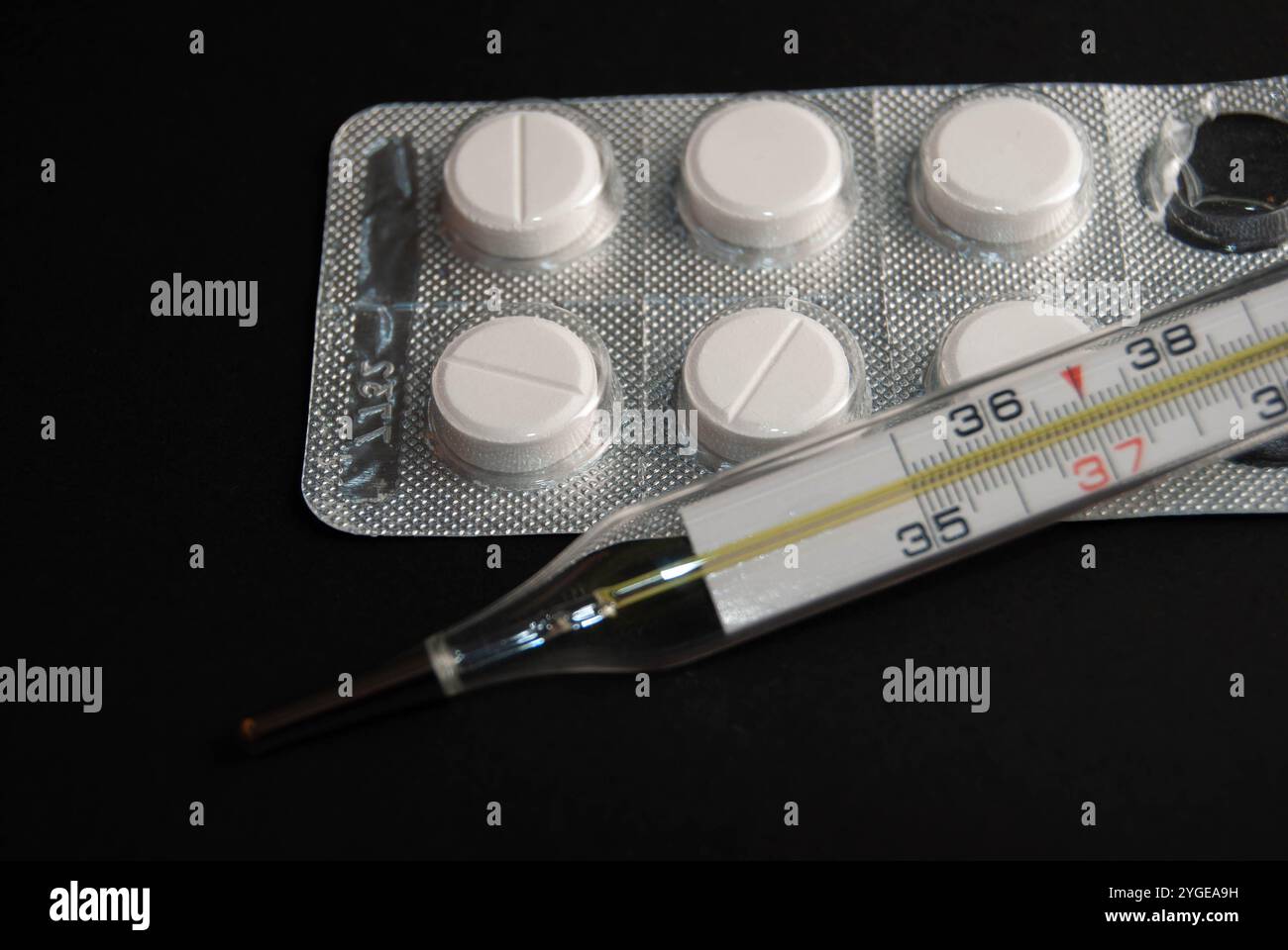 Eine Nahaufnahme eines Thermometers und Paracetamol-Pillen isoliert auf schwarzem Hintergrund, ideal für die Illustration von Gesundheit, Medizin und saisonaler Grippe. Stockfoto