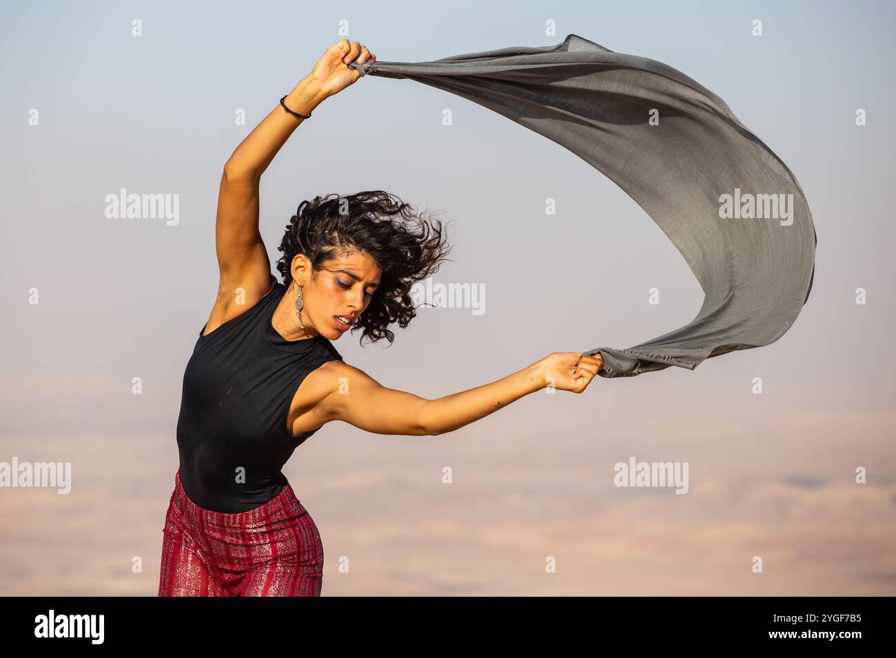 Wüstenbrise. Eine Tänzerin bewegt sich mit einem fließenden Schal anmutig gegen die weite Wüstenlandschaft, die während der Bewegung erfasst wird. Stockfoto
