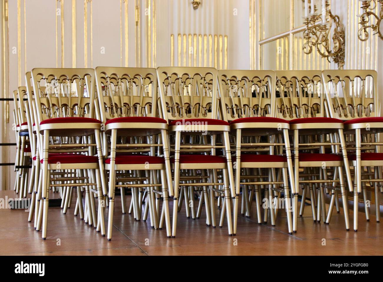 Wien, Österreich - 6. Oktober 2024: Gestapelte goldene Stühle mit roten Samtkissen im prunkvollen Ballsaal im Schloss Schönbrunn. Hochwertige Fotos Stockfoto