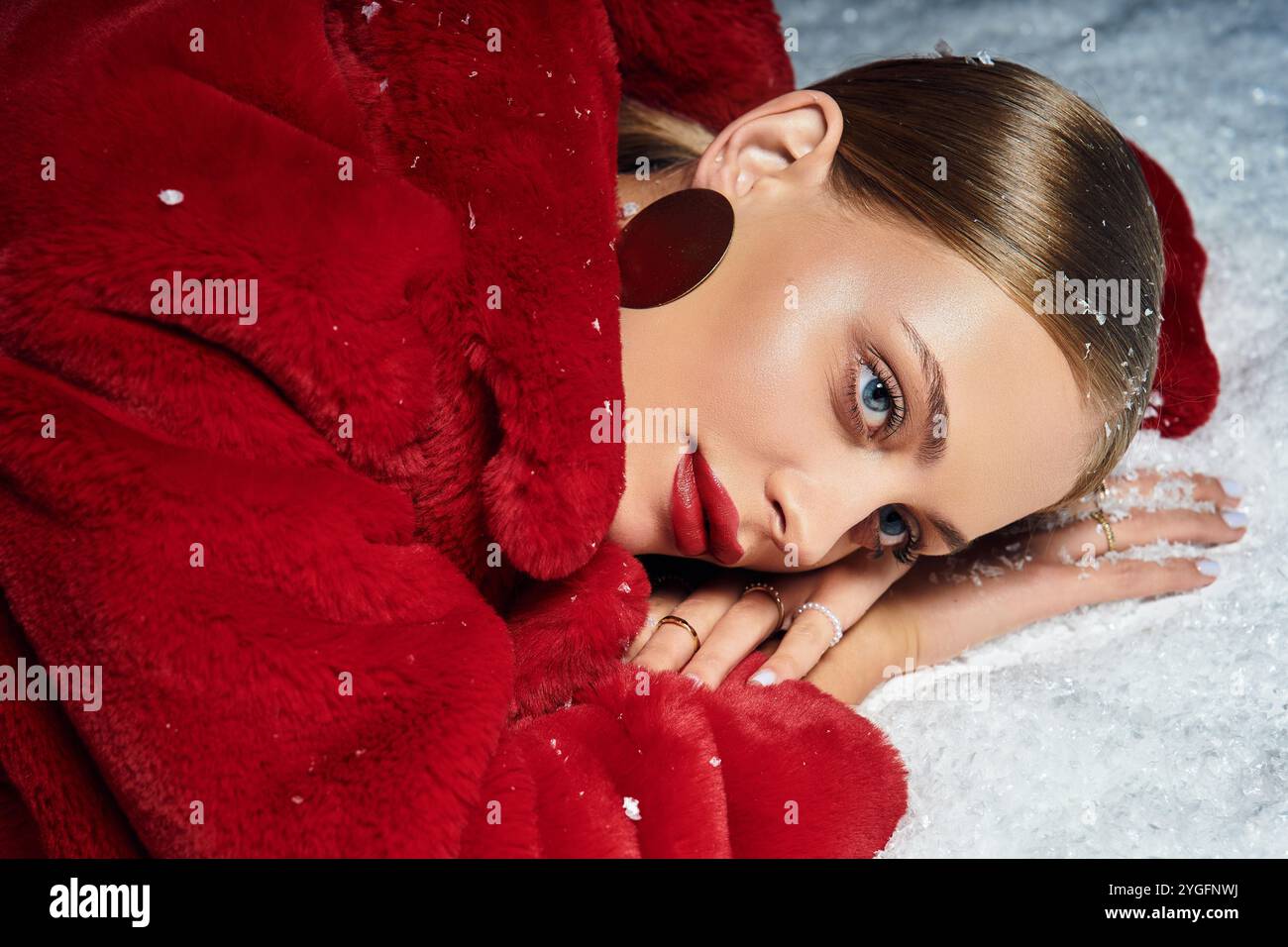 Eine junge Frau genießt einen friedlichen Moment, während sie sich im roten Mantel auf dem schneebedeckten Boden ausruht. Stockfoto